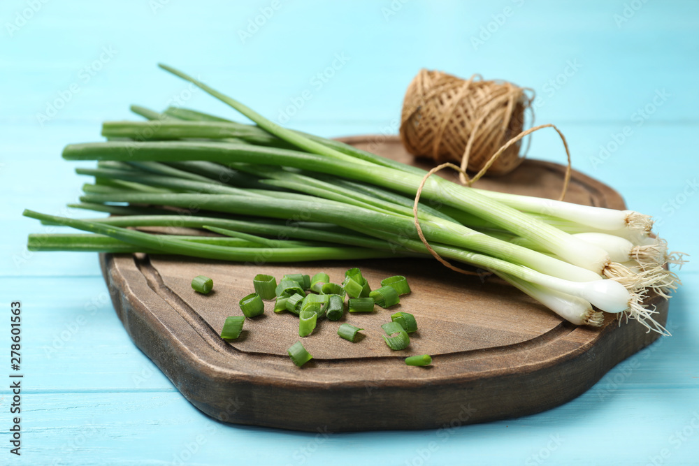 Wooden board with fresh green onions on light blue table Wooden board with fresh green onions on light blue table