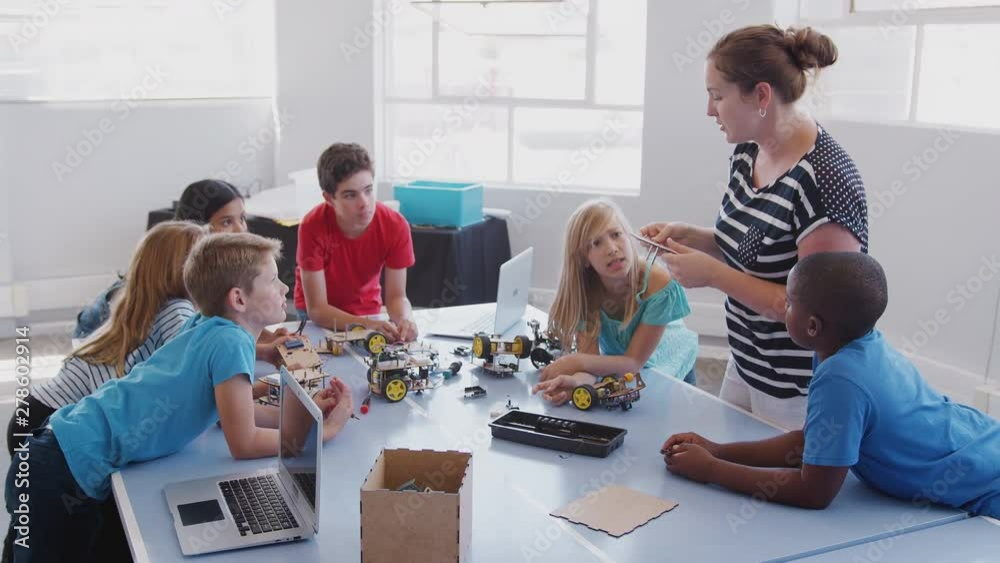 Students With Female Teacher In After School Computer Coding Class Learning To Program Robot Vehicle Students With Female Teacher In After School Computer Coding Class Learning To Program Robot Vehicle