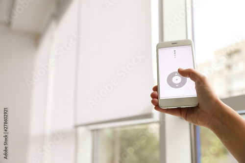 Woman using smart home application on phone to control window blinds indoors, closeup. Space for text photo
