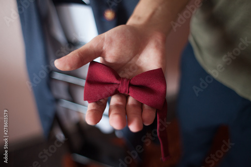 Groom getting dressed and preparing for the wedding, holding a red butterfly in his hands. Bow tie in the hands of the groom