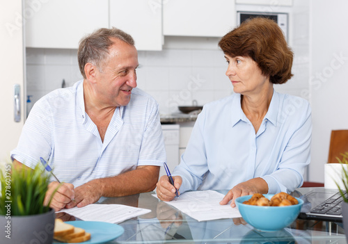 Smiling mature couple at table filling up documents at table in home
