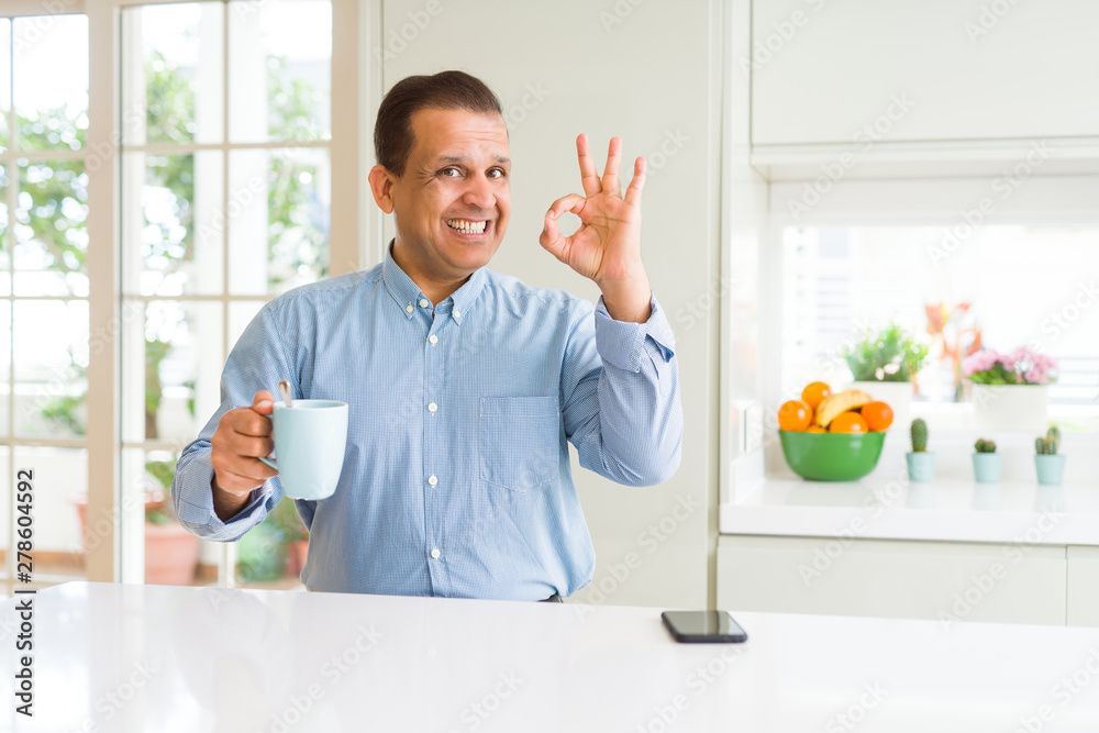 Middle age business man drinking coffee in the morning at home doing ok sign with fingers, excellent symbol Middle age business man drinking coffee in the morning at home doing ok sign with fingers, excellent symbol