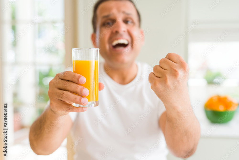 Middle age man drinking a glass of orange juice at home screaming proud and celebrating victory and success very excited, cheering emotion Middle age man drinking a glass of orange juice at home screaming proud and celebrating victory and success very excited, cheering emotion