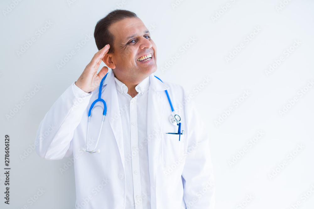 Middle age doctor man wearing stethoscope and medical coat over white background smiling with hand over ear listening an hearing to rumor or gossip. Deafness concept. Middle age doctor man wearing stethoscope and medical coat over white background smiling with hand over ear listening an hearing to rumor or gossip. Deafness concept.