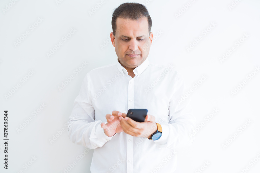 Middle age man using smartphone over white wall with a confident expression on smart face thinking serious Middle age man using smartphone over white wall with a confident expression on smart face thinking serious