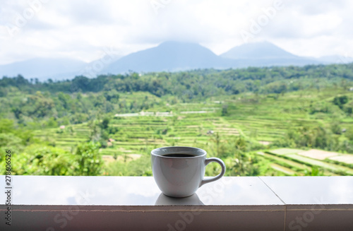 White mug of coffee stands on the background of rice fields