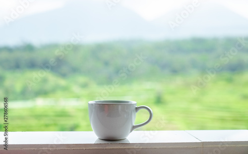 White mug of coffee stands on the background of rice fields