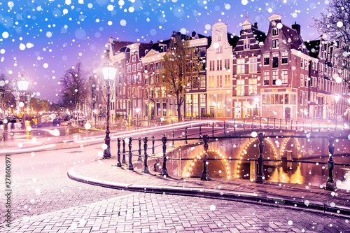Traditional Dutch old houses and bridges on the canals in Amsterdam on a snowy winter night, The Netherlands