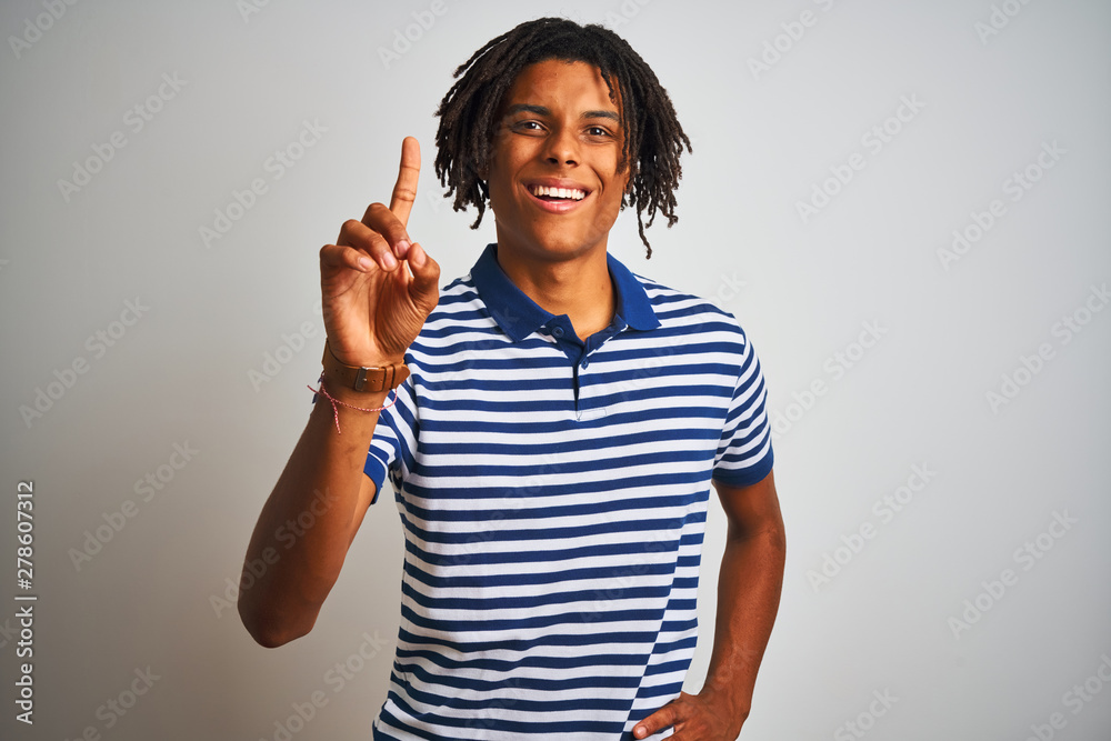 Afro man with dreadlocks wearing striped blue polo standing over isolated white background pointing finger up with successful idea. Exited and happy. Number one. Afro man with dreadlocks wearing striped blue polo standing over isolated white background pointing finger up with successful idea. Exited and happy. Number one.