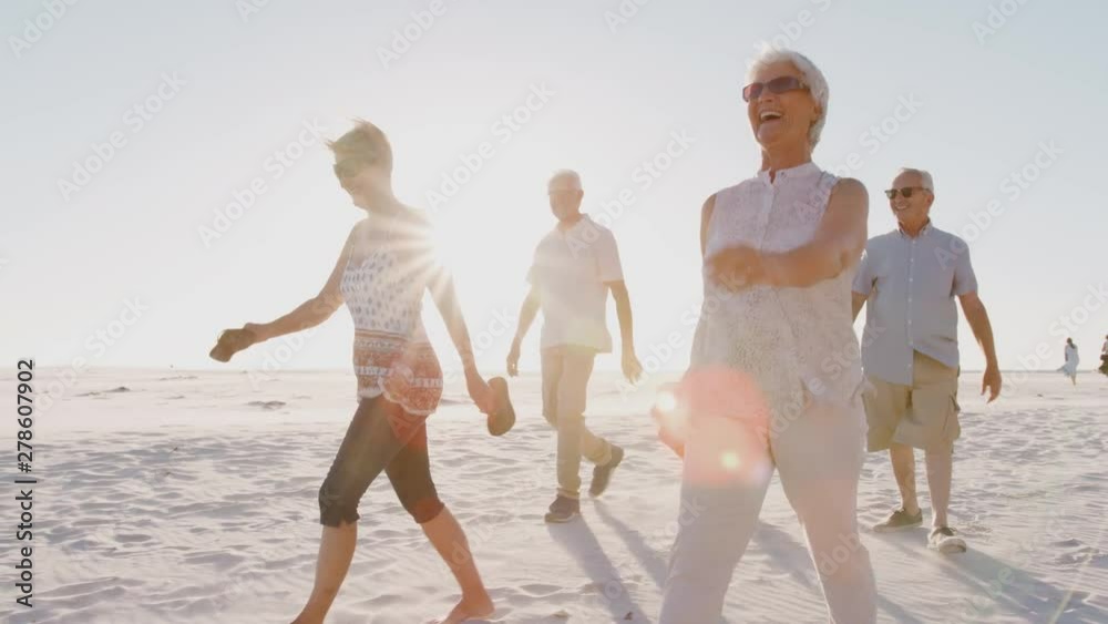 Group Of Senior Friends Walking Along Sandy Beach On Summer Group Vacation 