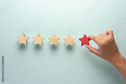 The concept of feedback of five stars. The hand adds a red star to the four ordinary ones.