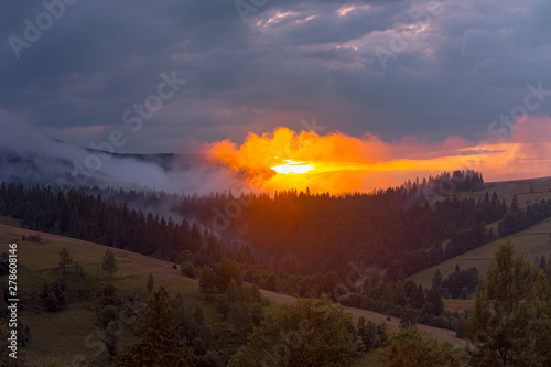 Bright sunset over foggy mountains. Vivid sun through the clouds over mountains slopes, covered with spruce forest. Carpathian mountains. Ukraine. © stone36