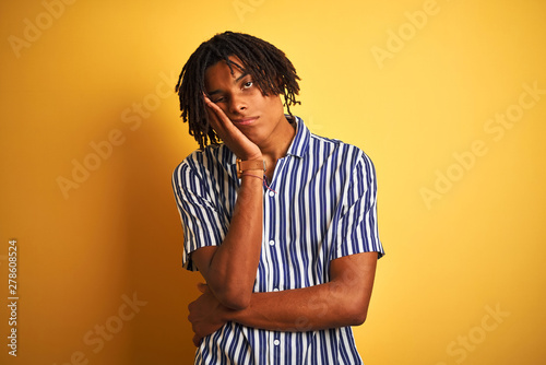 Afro man with dreadlocks wearing casual striped t-shirt over isolated yellow background thinking looking tired and bored with depression problems with crossed arms. © Krakenimages.com
