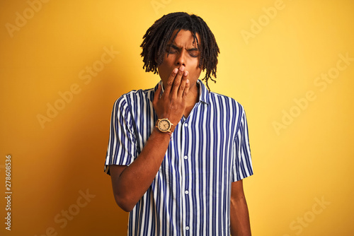 Afro man with dreadlocks wearing casual striped t-shirt over isolated yellow background bored yawning tired covering mouth with hand. Restless and sleepiness. © Krakenimages.com
