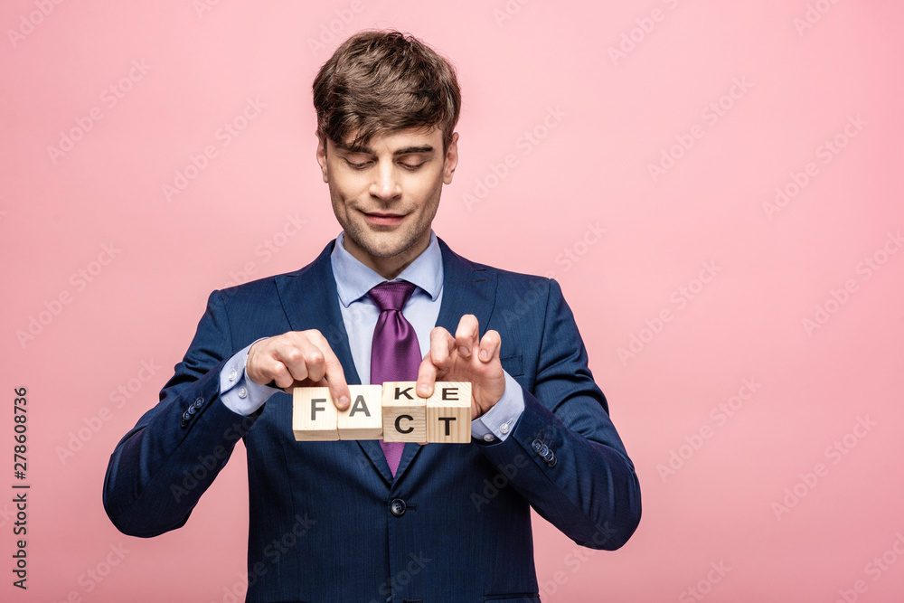smiling man holding wooden cubes with fake fact inscription isolated on pink smiling man holding wooden cubes with fake fact inscription isolated on pink