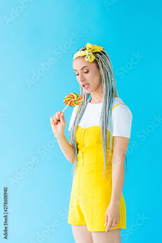 girl with dreadlocks and headband holding lollipop on turquoise