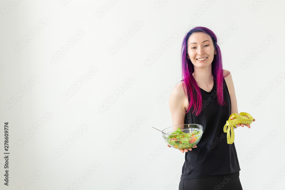 Unidentified young girl hipster with purple hair measures her waist with a measuring tape on a white background with copyspace. Healthy lifestyle concept. Unidentified young girl hipster with purple hair measures her waist with a measuring tape on a white background with copyspace. Healthy lifestyle concept.