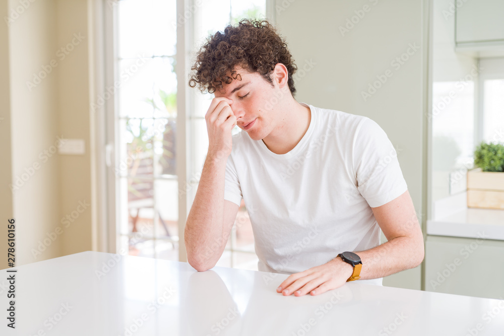 Young handsome man wearing white t-shirt at home tired rubbing nose and eyes feeling fatigue and headache. Stress and frustration concept.