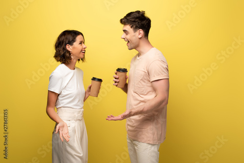 smiling man and woman talking while holding paper cups on yellow background