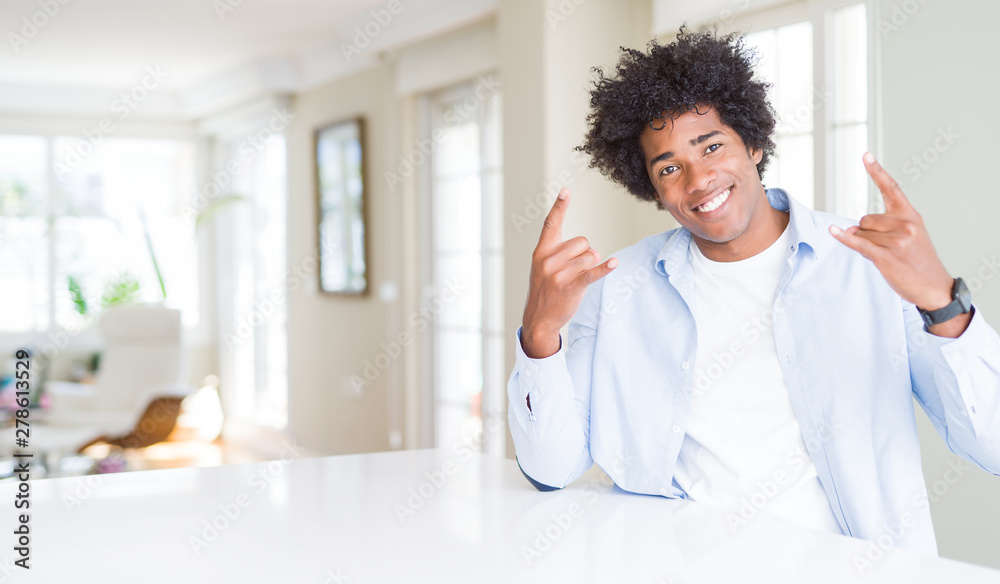 African American man at home shouting with crazy expression doing rock symbol with hands up. Music star. Heavy concept. African American man at home shouting with crazy expression doing rock symbol with hands up. Music star. Heavy concept.