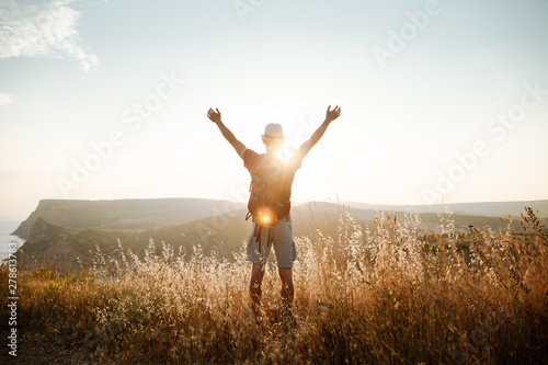 A guy stands in the mountains and raised his hands to the sky