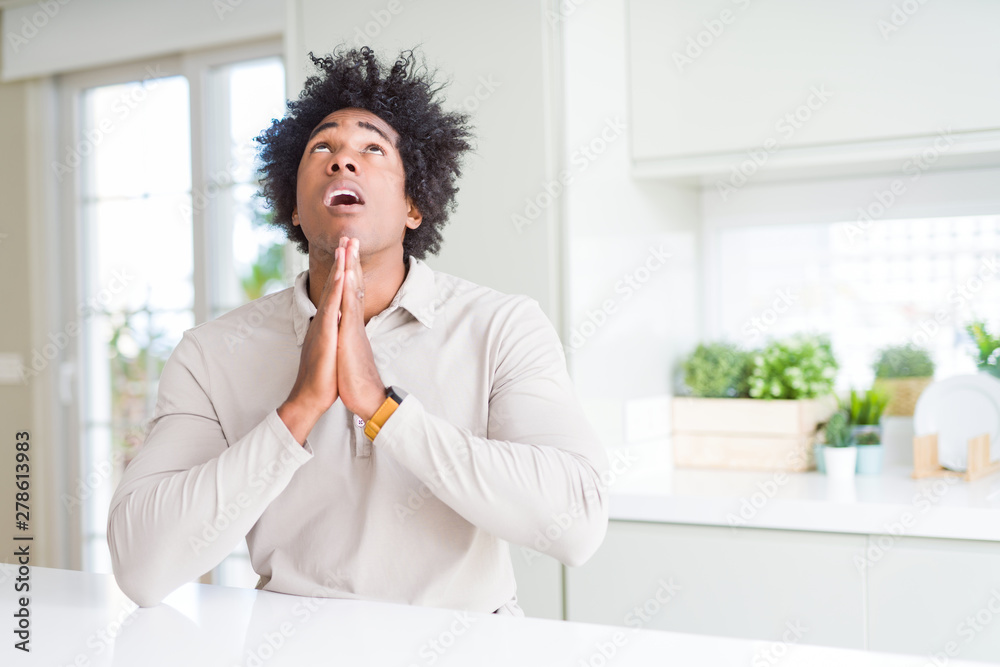 African American man at home begging and praying with hands together with hope expression on face very emotional and worried. Asking for forgiveness. Religion concept. African American man at home begging and praying with hands together with hope expression on face very emotional and worried. Asking for forgiveness. Religion concept.