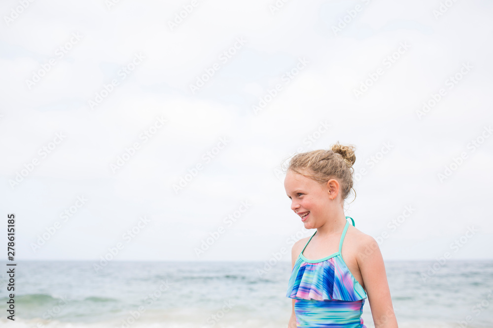 Smiling Young Blonde Curly Haired Girl in Bathing Suit, Ocean Behind Smiling Young Blonde Curly Haired Girl in Bathing Suit, Ocean Behind