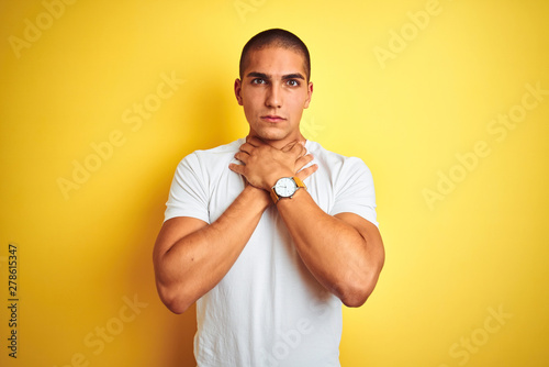 Young caucasian man wearing casual white t-shirt over yellow isolated background shouting and suffocate because painful strangle. Health problem. Asphyxiate and suicide concept.