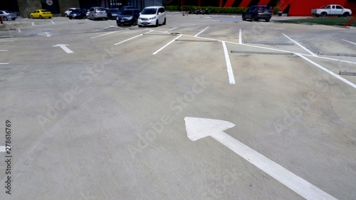 Traffic arrow sign with white lines and concrete wheel stoppers in parking lot or outdoor car park area, selective focus
