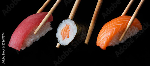 Slika na platnu Traditional japanese sushi pieces placed between chopsticks, separated on black