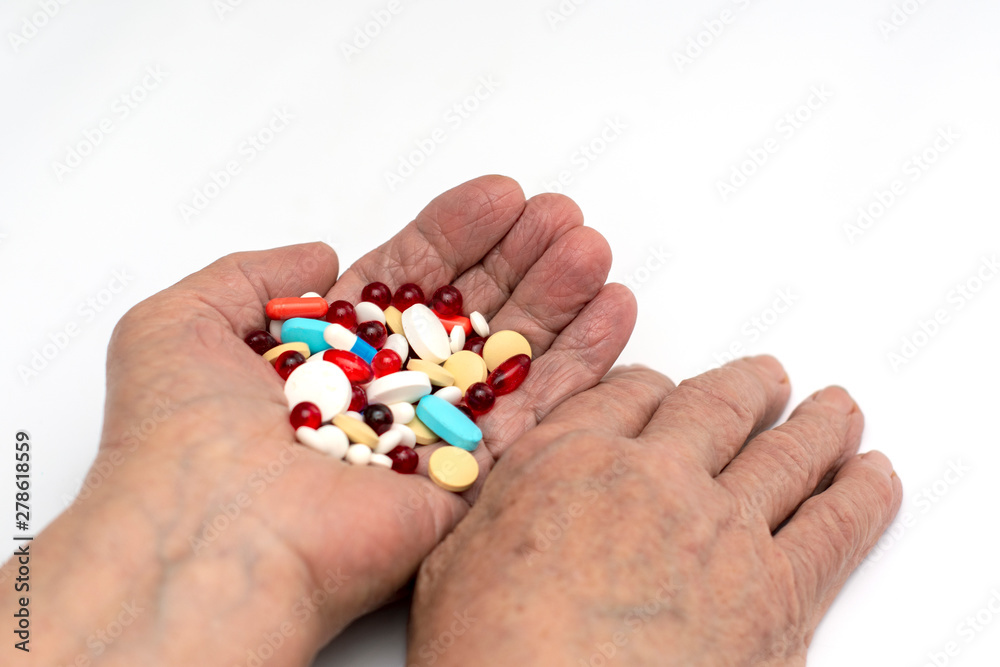 Old hands hold multicolored medical pills and tablets for ingestion from diseases on a white background. Old hands hold multicolored medical pills and tablets for ingestion from diseases on a white background.