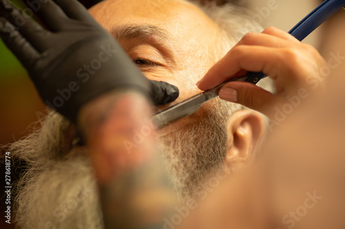 Master cuts hair and beard of men in the barbershop, hairdresser makes hairstyle for a old man