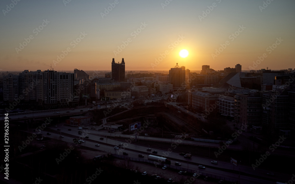 Obraz premium Aerial shot of a late evening in Novosibirsk. The sun will soon set below the horizon. One can see the silhouettes of buildings against the sunset sky.