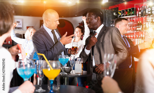 Two cheerful male colleagues enjoying corporate bar party, drink