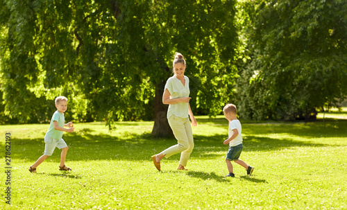family, leisure and people concept - happy mother and two little sons running and playing catch game at summer park