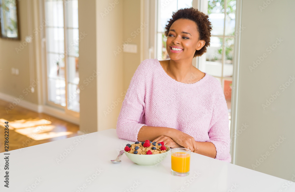 Young african american woman having healthy breakfast in the morning at home looking away to side with smile on face, natural expression. Laughing confident.