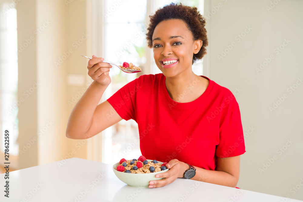 Young beautiful african american woman with afro hair eating healthy wholemeal cereals and berries as healthy breakfast