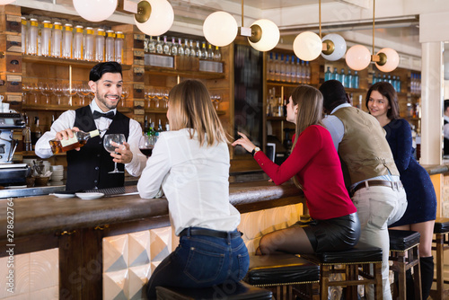Barman is servicing young people who are relaxing in bar indoor. © JackF