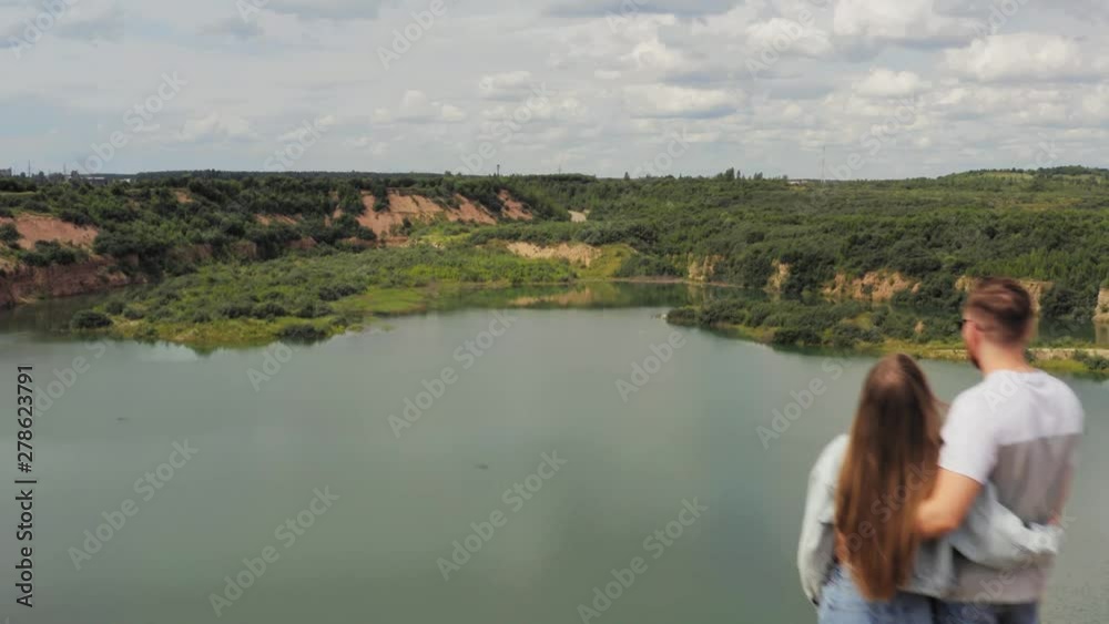 Couple is standing on a mountain cliff by the lake. Couple in love hugging against the background of beautiful views of nature. Aerial. 4K Couple is standing on a mountain cliff by the lake. Couple in love hugging against the background of beautiful views of nature. Aerial. 4K