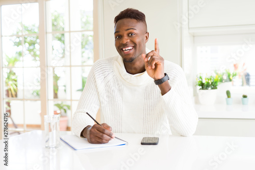 African american student man writing on a paper using a pencil surprised with an idea or question pointing finger with happy face, number one