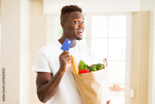African american man holding paper bag full of groceries and holding credit card as payment
