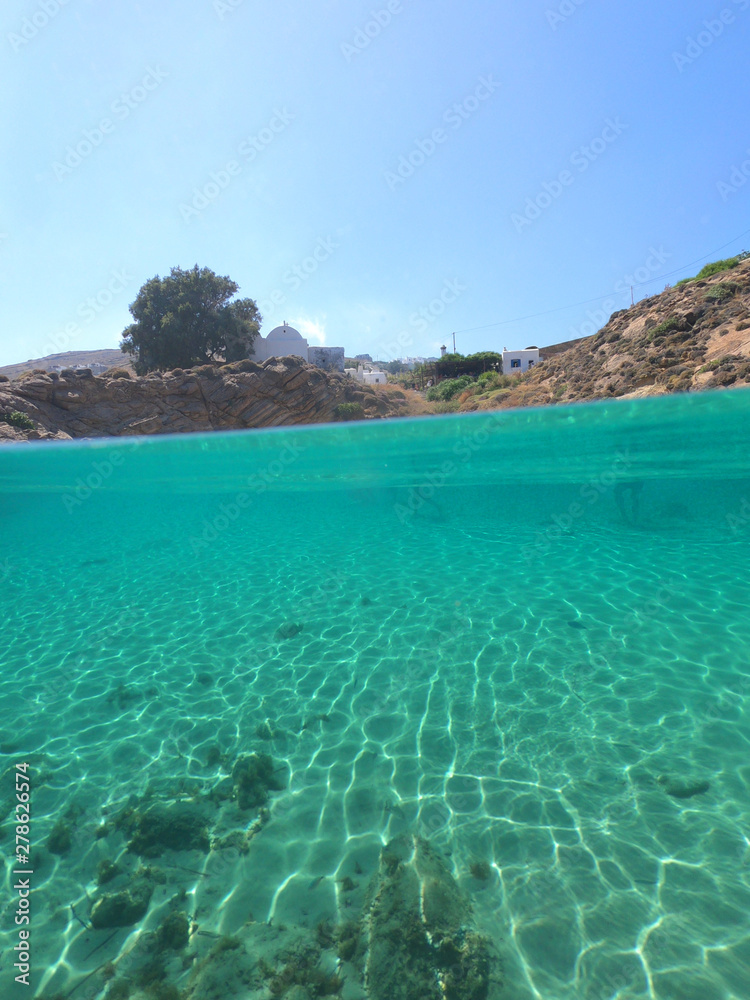 Split of above and underwater photo of iconic and beautiful small cove and sandy clear turquoise beach of Agios Sostis, Mykonos island, Greece