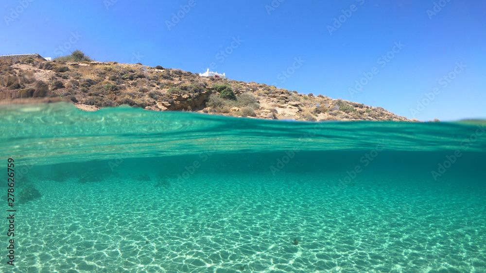Split of above and underwater photo of iconic and beautiful small cove and sandy clear turquoise beach of Agios Sostis, Mykonos island, Greece