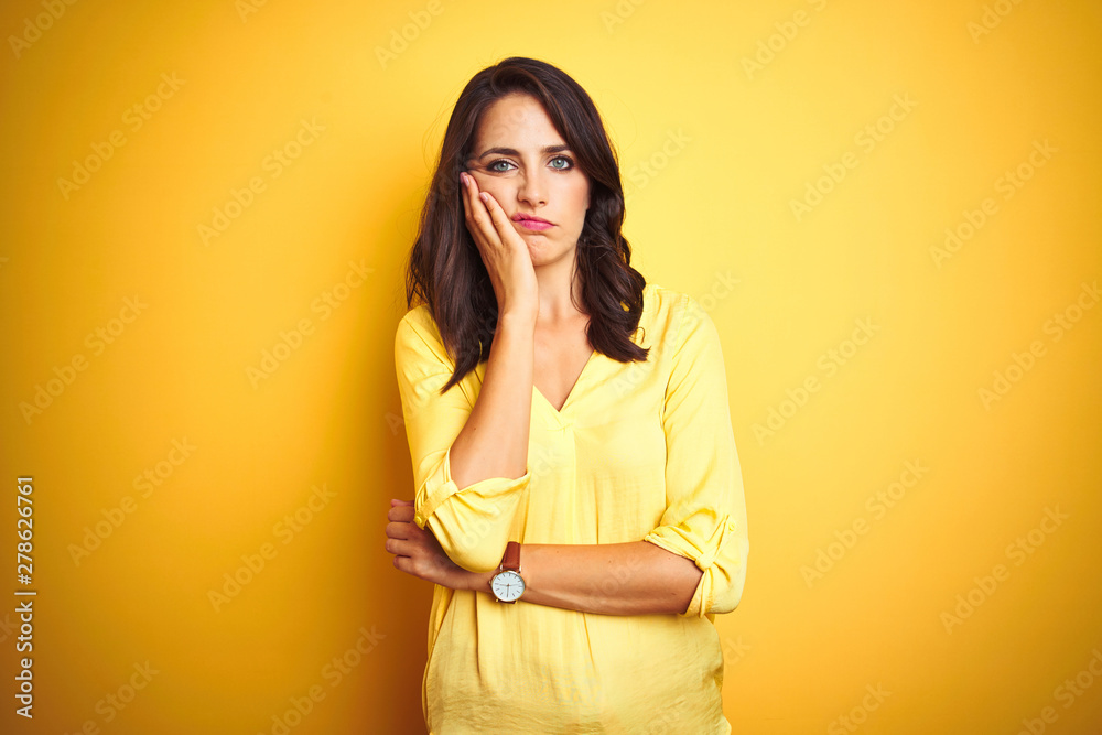 Beautiful elegant woman standing over yellow isolated background thinking looking tired and bored with depression problems with crossed arms.
