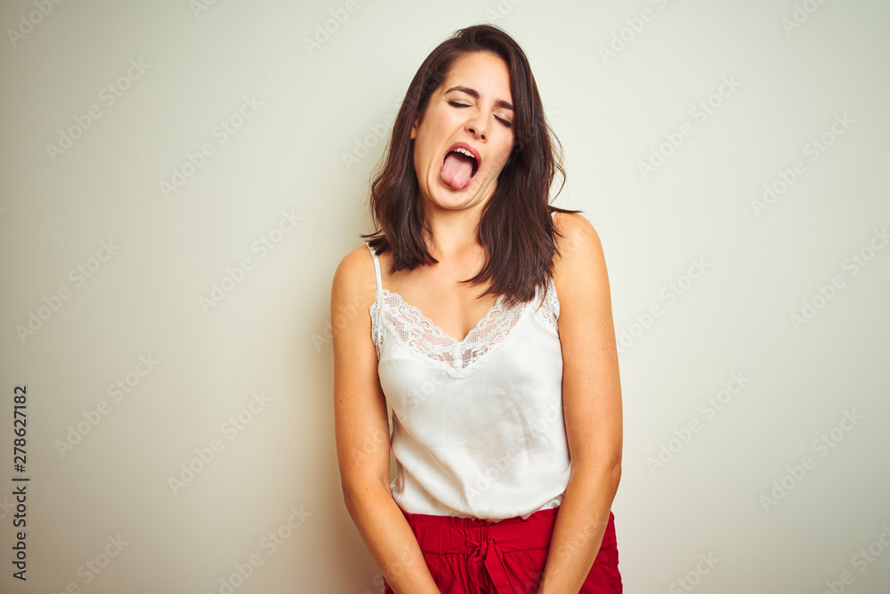 Young beautiful woman wearing t-shirt standing over white isolated background sticking tongue out happy with funny expression. Emotion concept. Young beautiful woman wearing t-shirt standing over white isolated background sticking tongue out happy with funny expression. Emotion concept.