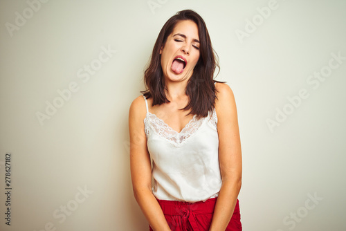 Young beautiful woman wearing t-shirt standing over white isolated background sticking tongue out happy with funny expression. Emotion concept.