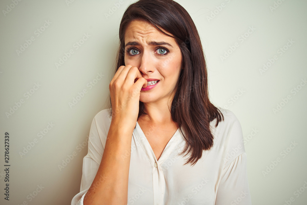 Young beautiful woman wearing casual shirt standing over white isolated background looking stressed and nervous with hands on mouth biting nails. Anxiety problem. Young beautiful woman wearing casual shirt standing over white isolated background looking stressed and nervous with hands on mouth biting nails. Anxiety problem.