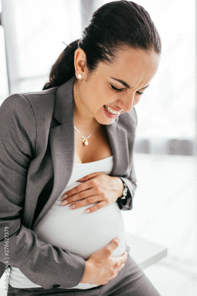 pregnant woman enduring pain and sitting on table in office pregnant woman enduring pain and sitting on table in office