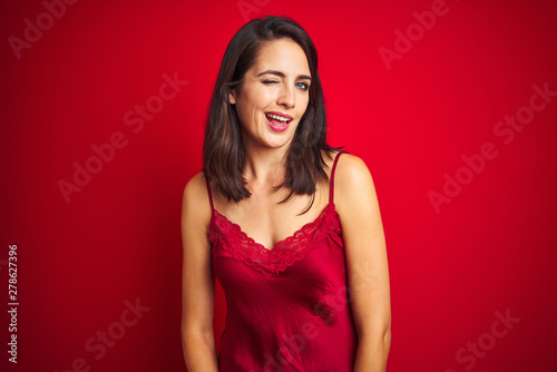 Young beautiful woman wearing sexy lingerie over red isolated background winking looking at the camera with sexy expression, cheerful and happy face.