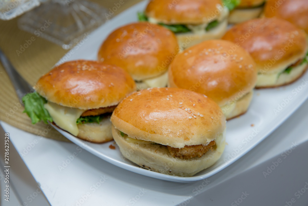 Beautifully decorated catering banquet table with different hamburgers burgers sandwiches on a plate on corporate birthday . Mini or Small Burger Canape in Luxury Restaurant for Brunch Time .